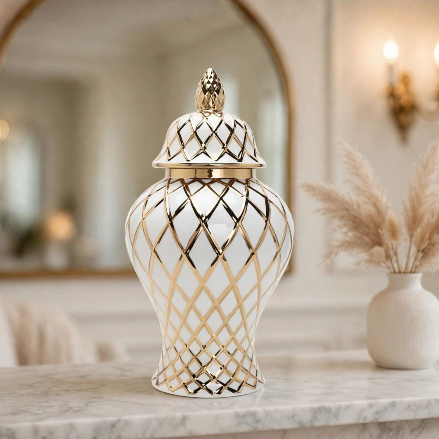 A white ceramic lidded jar with a gold geometric lattice pattern and a gold pineapple finial, displayed on a marble countertop in a warm, elegant interior setting.