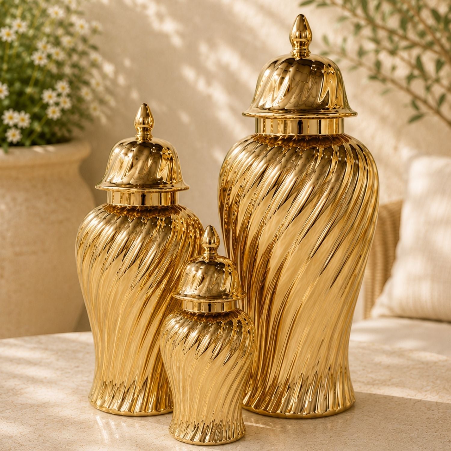 Three metallic gold decorative urns with ribbed swirl patterns and domed lids, arranged on a light stone surface with a softly blurred indoor background.
