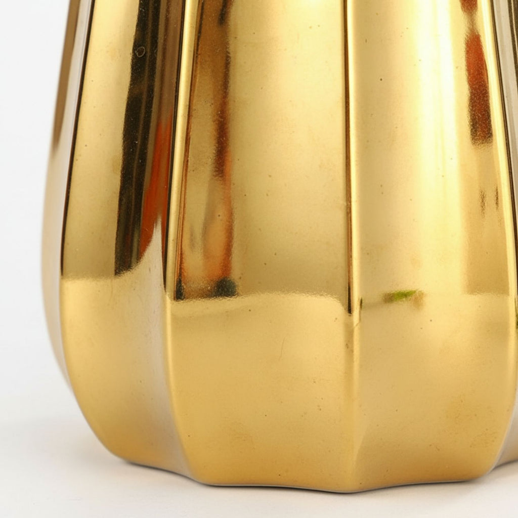 Close-up of a shiny metallic gold object with vertical fluted panels and a rounded base, photographed against a plain white background.