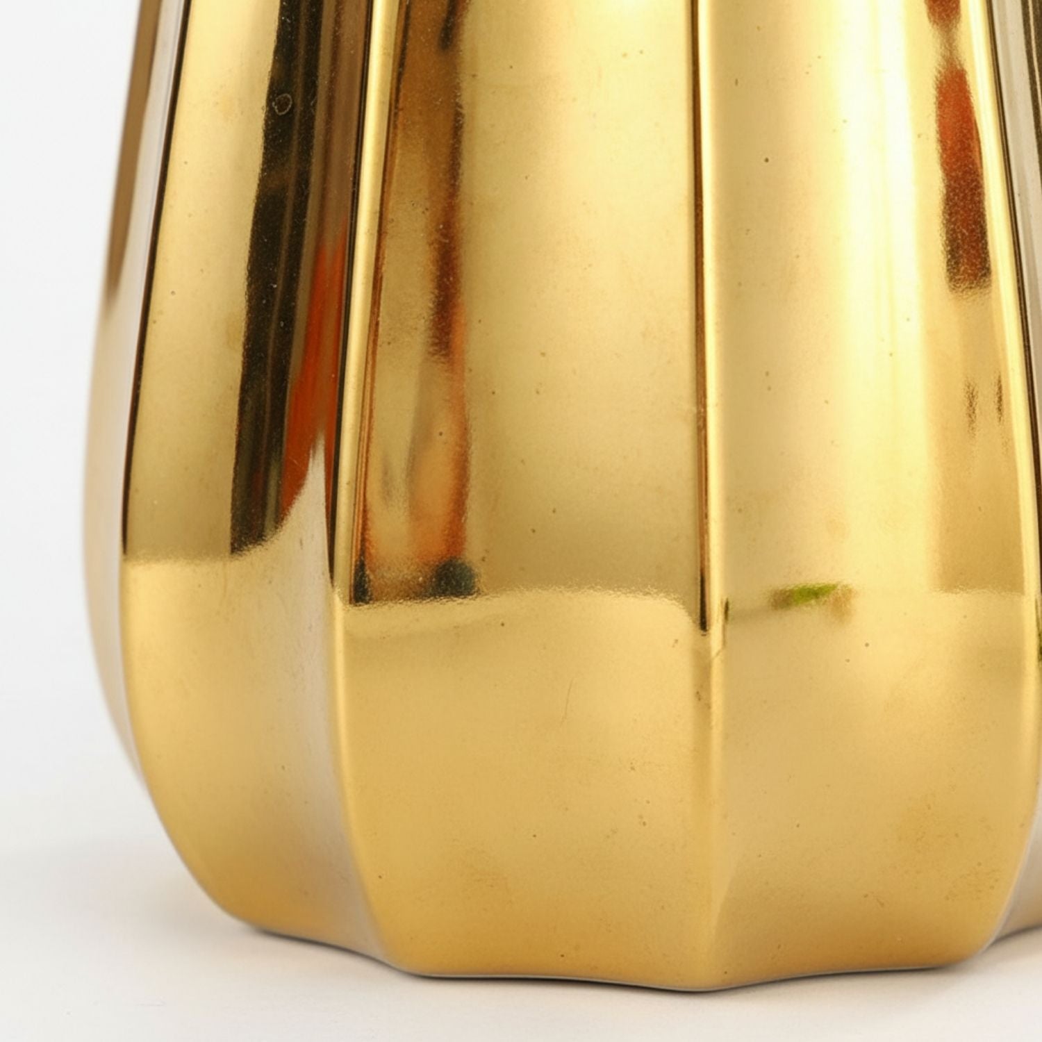 Close-up of a shiny metallic gold object with vertical fluted panels and a rounded base, photographed against a plain white background.