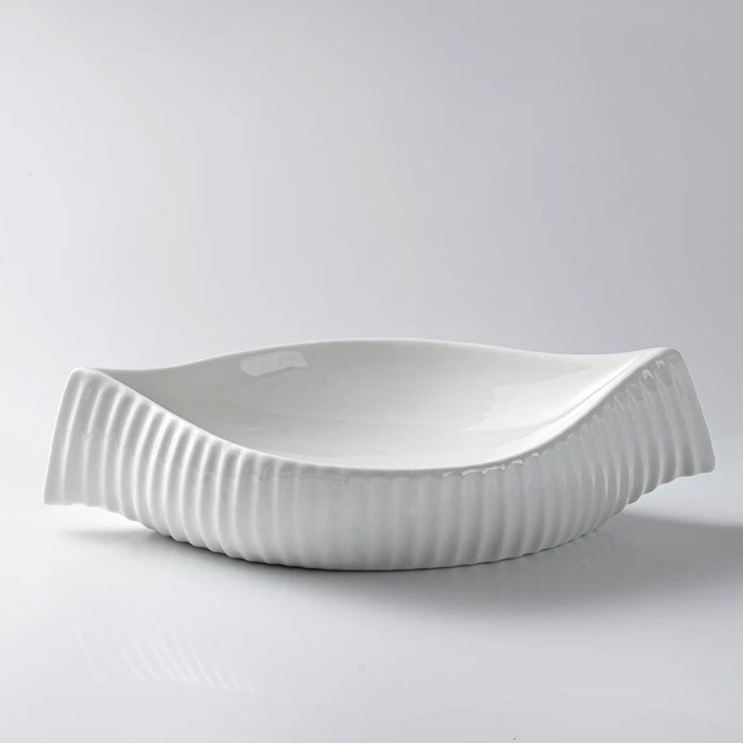 A white ceramic serving bowl with a ribbed, wavy rim, photographed on a clean light gray studio background.