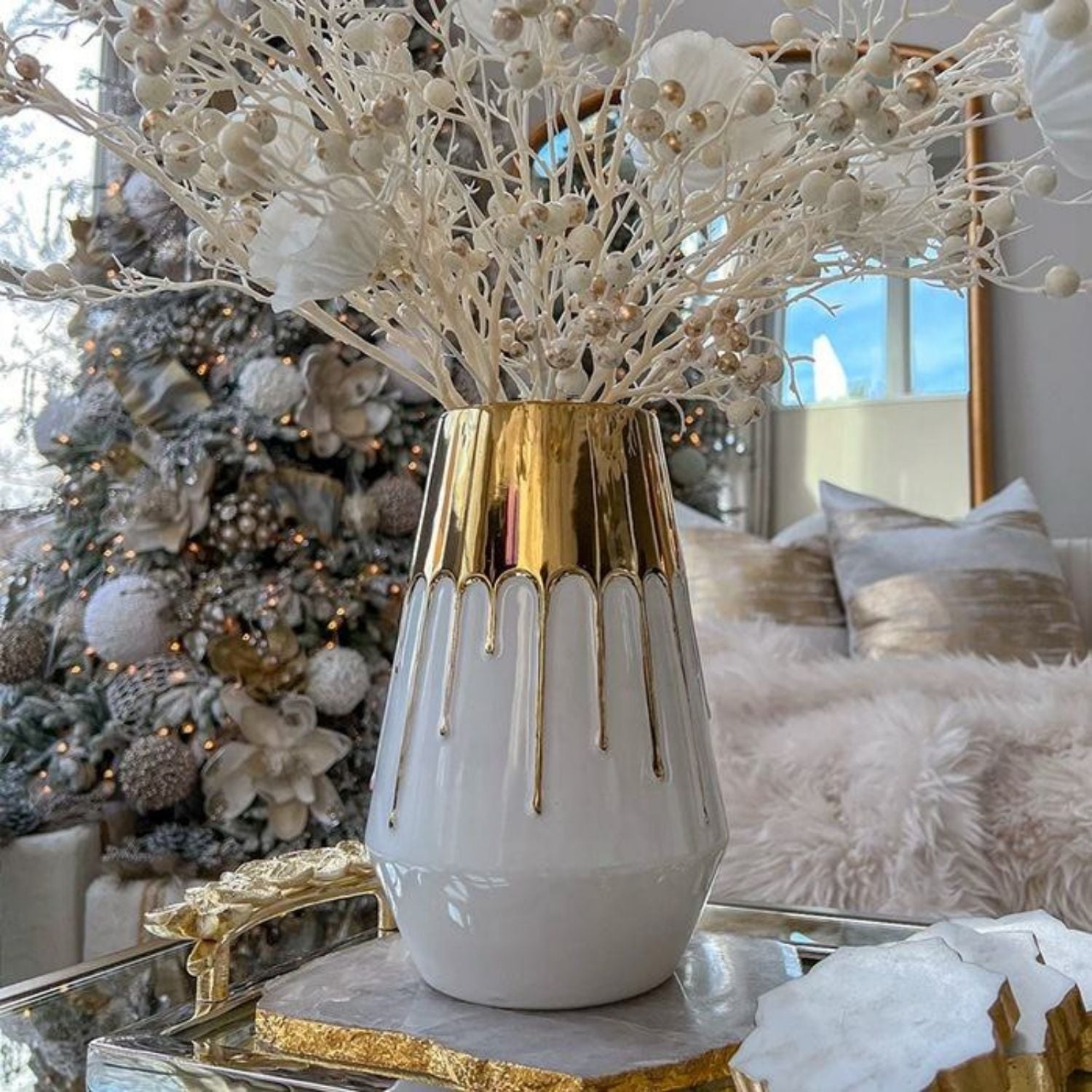Decorative white vase with gold accents on a table in a festive room with Christmas tree and pillows.