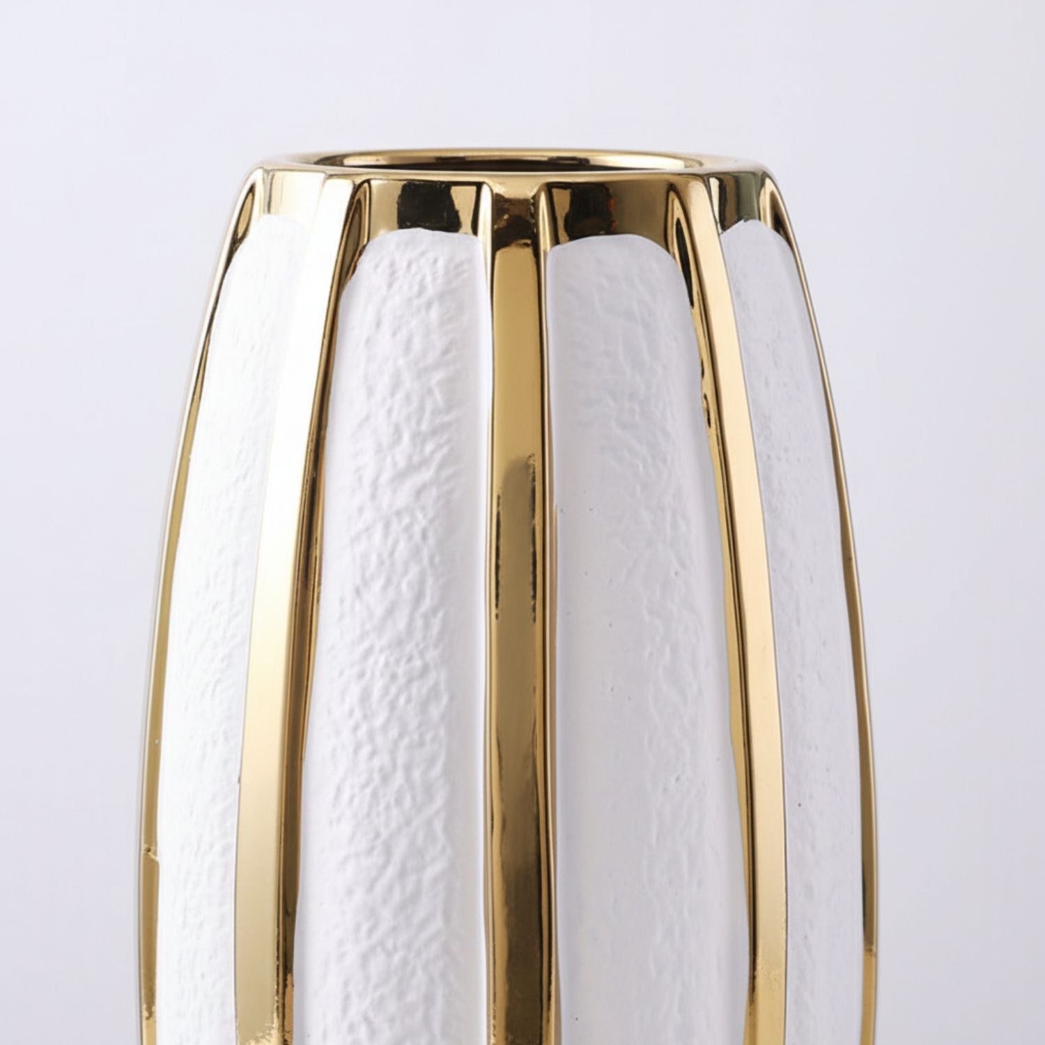 A close-up of a modern vase with a glossy gold metallic frame and textured white vertical panels, set against a clean light gray background.