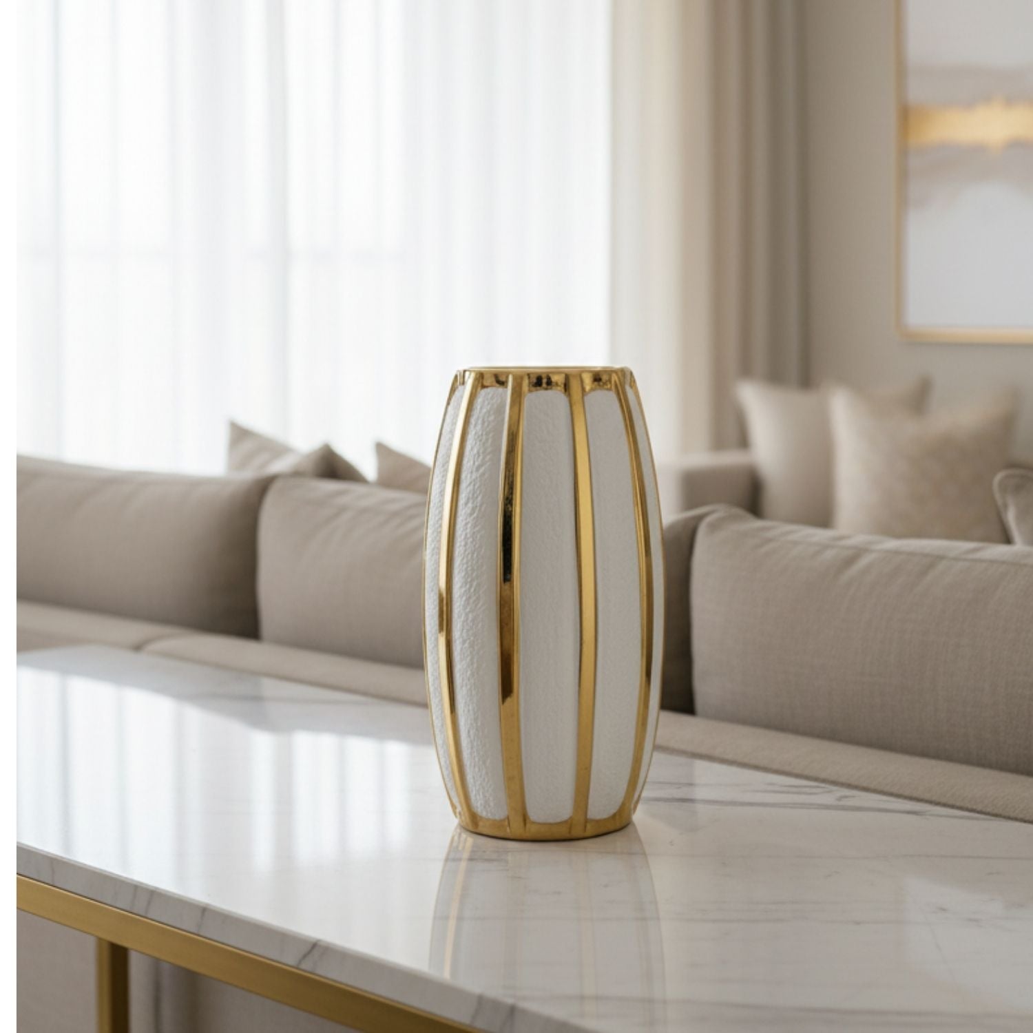 A modern ribbed ceramic vase with a white textured body and polished gold vertical bars, displayed on a marble-top table in a contemporary living room setting.