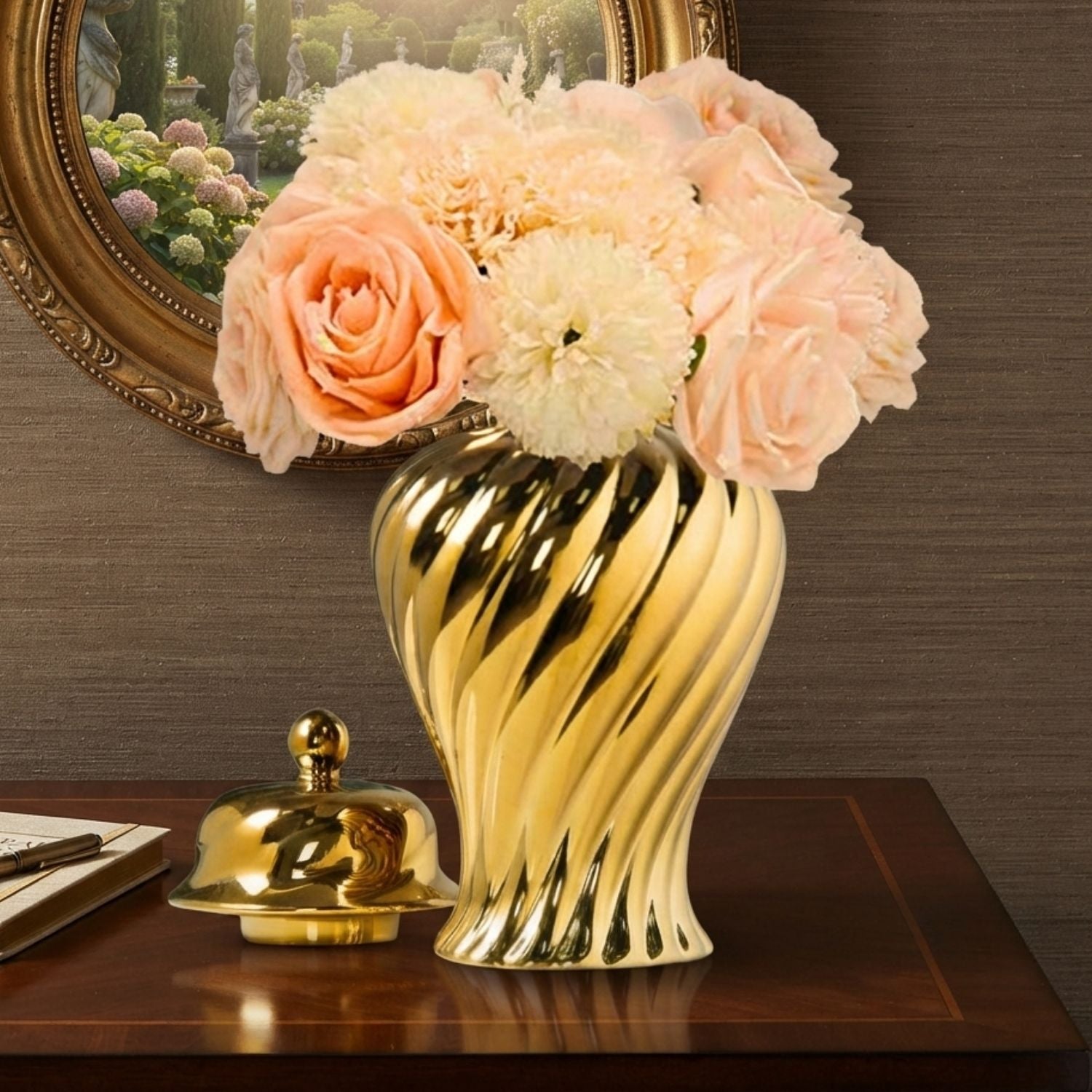 A shiny gold ribbed ceramic vase filled with peach and cream artificial roses, displayed on a dark wooden table next to a small gold decorative object, with a brown textured wall and a framed mirror in the background.