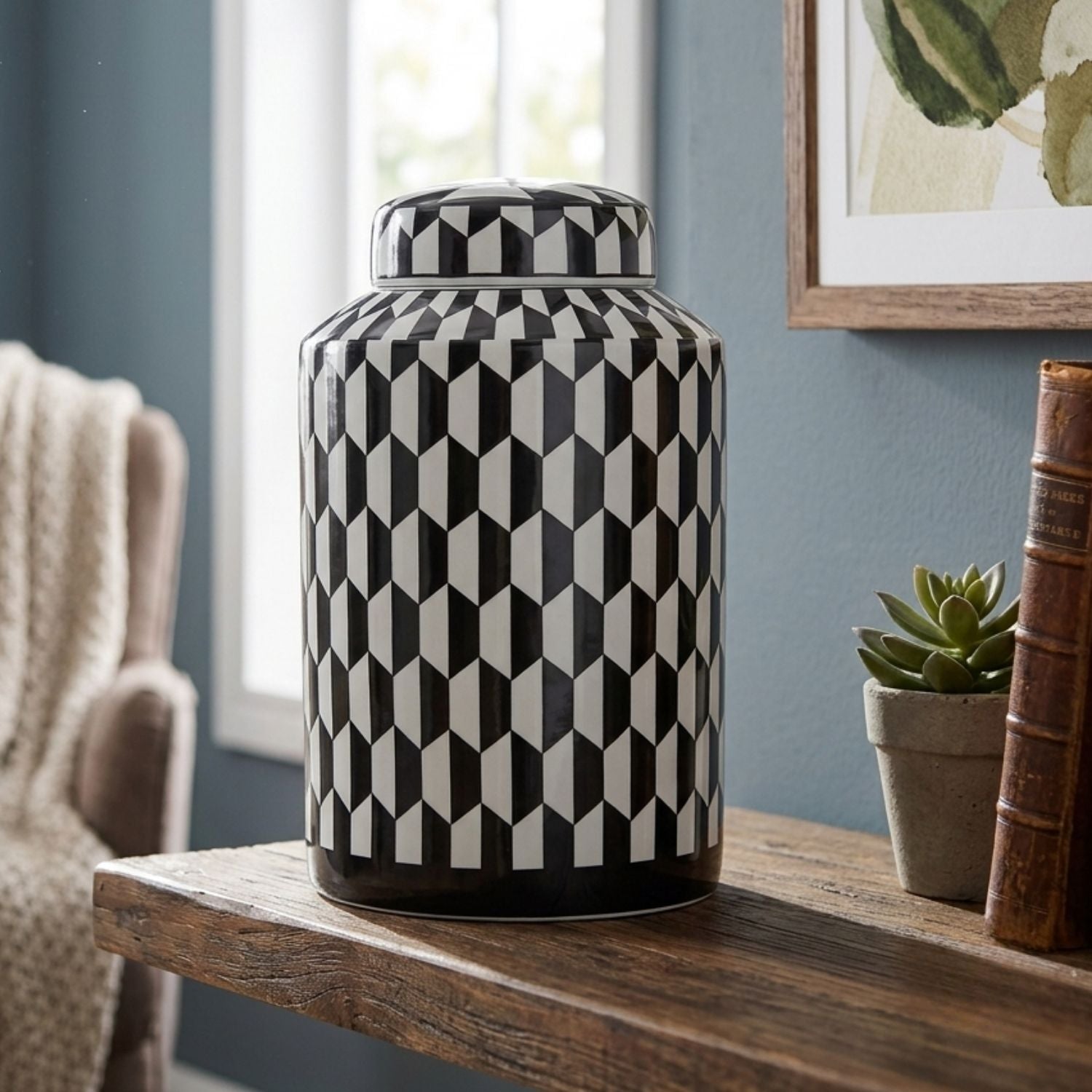 A black and white geometric patterned ceramic canister with a matching lid, displayed on a rustic wooden table in a styled room setting.