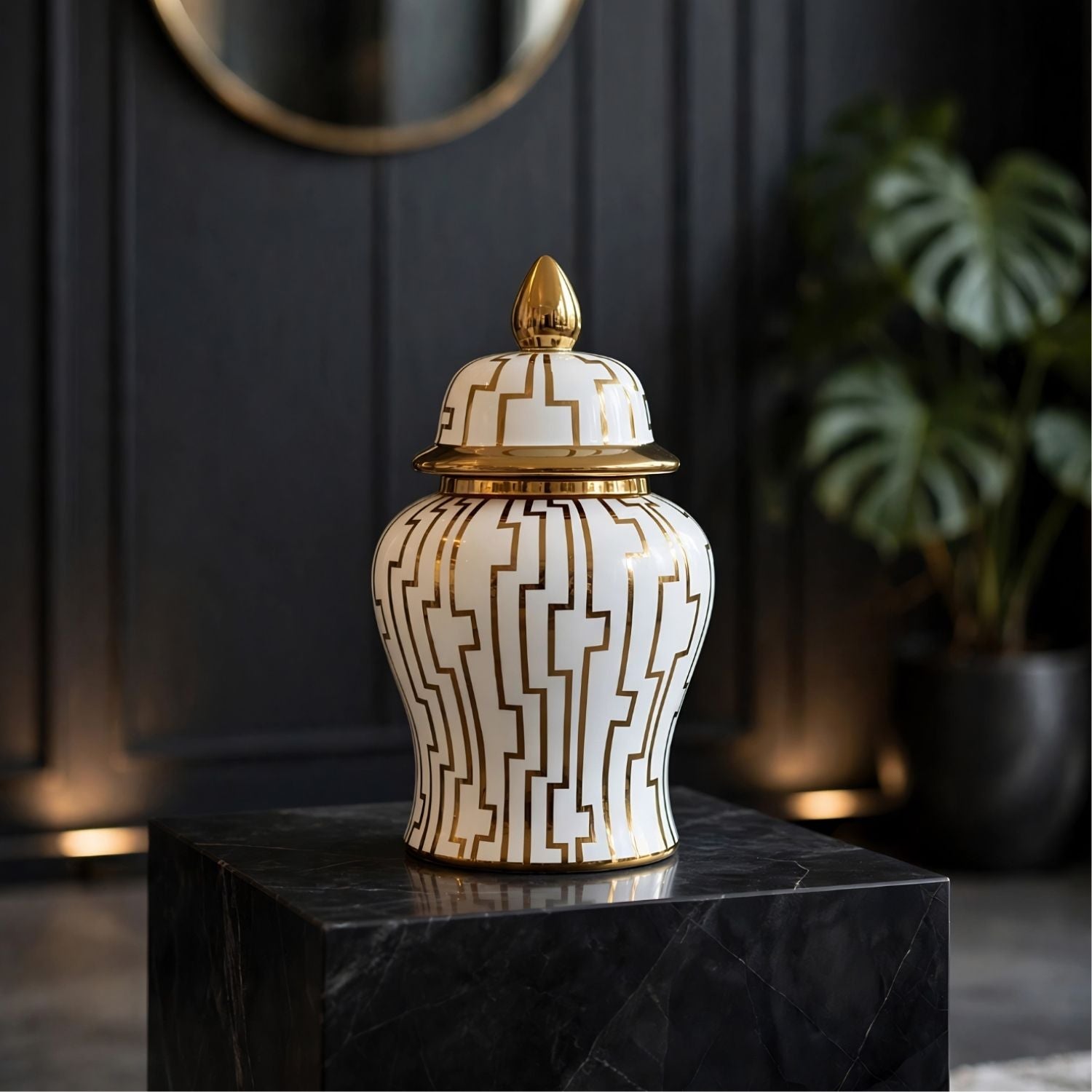 A decorative ceramic ginger jar with a white body, gold geometric pattern, and gold lid finial, displayed on a black marble pedestal in a dark interior setting.