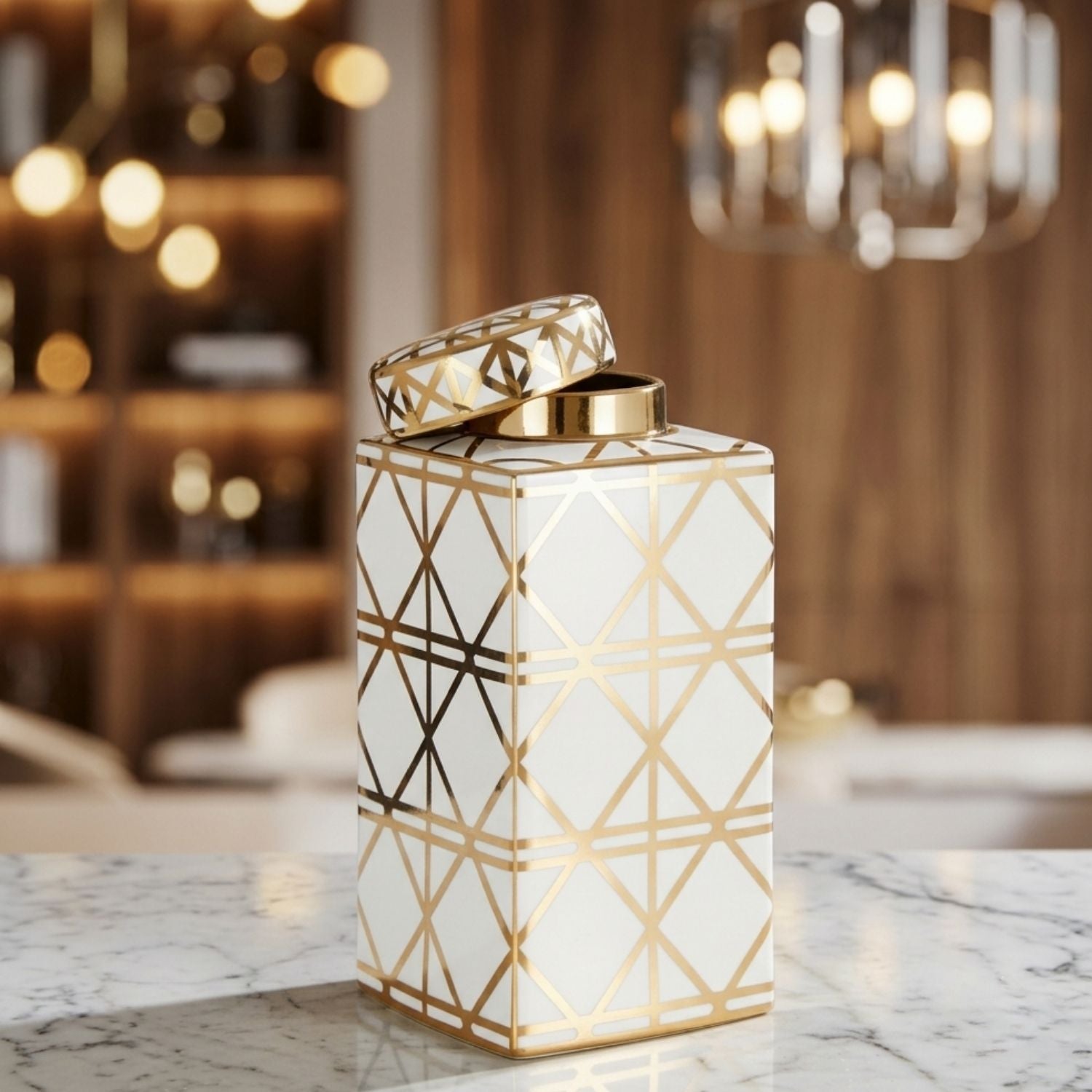 A white ceramic canister with a gold geometric line pattern and a matching lid, displayed on a marble countertop in a warm, blurred interior setting.