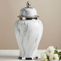 A white ceramic urn with a gray marble swirl pattern and polished silver-tone metal trim and lid, displayed on a white marble surface next to white roses against a beige background.
