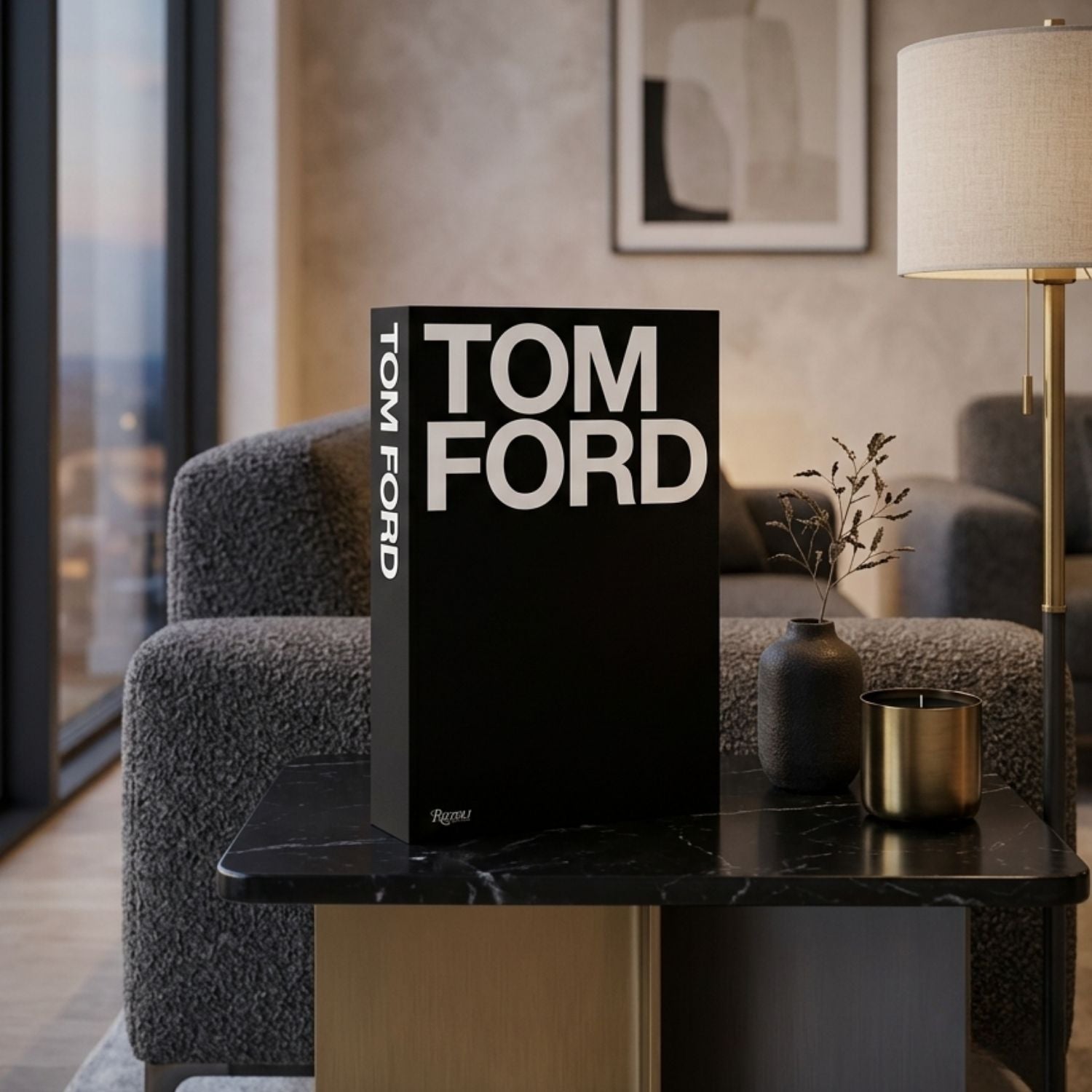 A black hardcover book titled 'TOM FORD' with bold white lettering stands upright on a dark marble-topped side table in a modern living room setting.