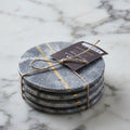 A set of four round gray marble coasters tied together with twine and a small product tag, placed on a white marble surface.