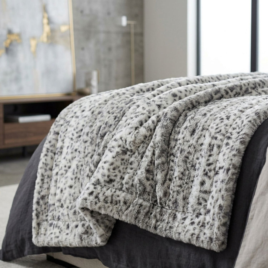 A plush faux-fur style throw blanket with a gray and white leopard print pattern draped over a bed in a modern bedroom setting.