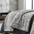 A plush faux-fur style throw blanket with a gray and white leopard print pattern draped over a bed in a modern bedroom setting.