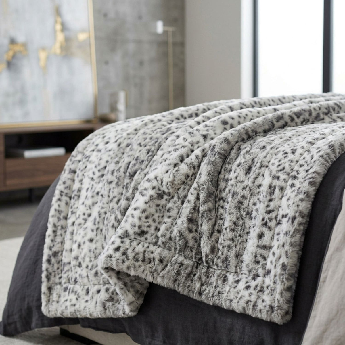 A plush faux-fur style throw blanket with a gray and white leopard print pattern draped over a bed in a modern bedroom setting.