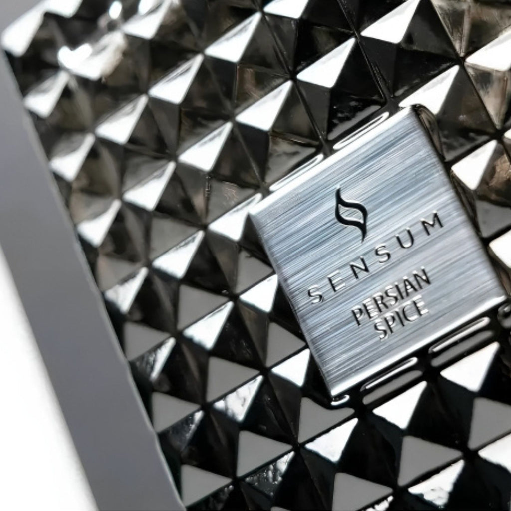 Close-up of a metallic silver Sensum Persian Spice product box or label placed on a glossy black geometric pyramid-patterned surface.