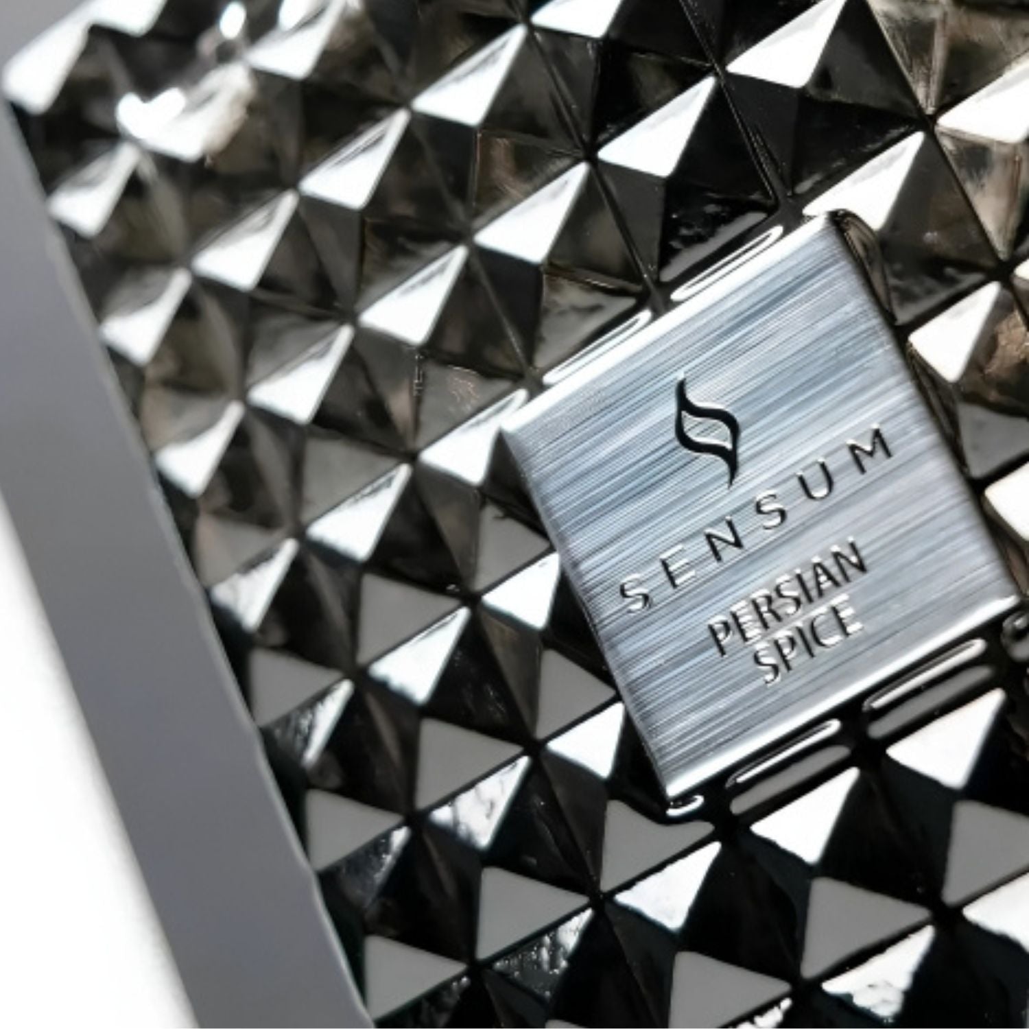 Close-up of a metallic silver Sensum Persian Spice product box or label placed on a glossy black geometric pyramid-patterned surface.