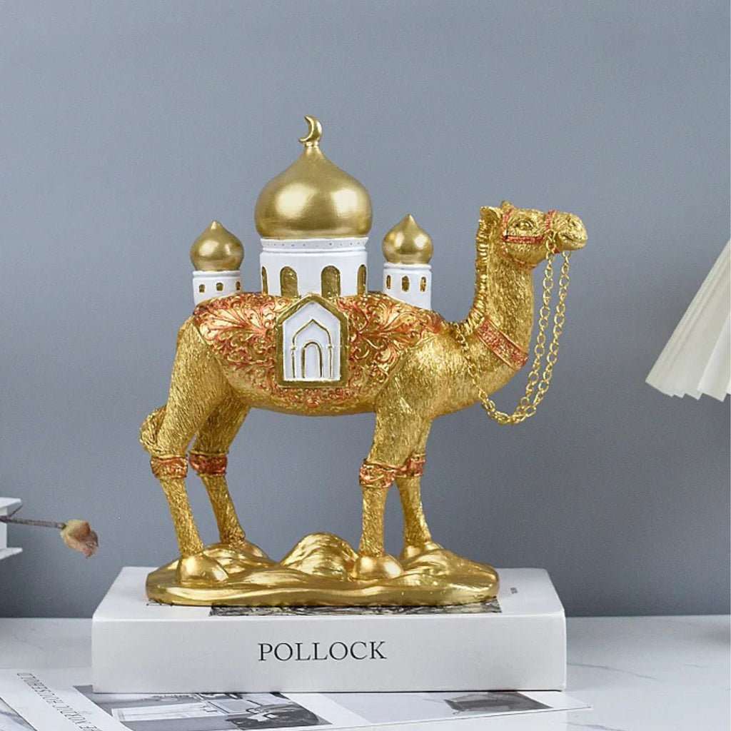 A decorative camel figurine in metallic gold with red and white embroidered details, standing on a white pedestal labeled POLLOCK against a soft gray background.