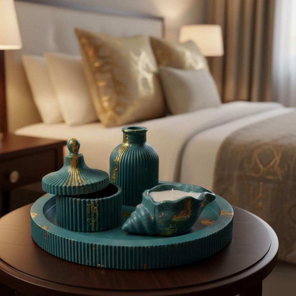 A teal and gold decorative ceramic set arranged on a round tray on a wooden table, with a softly blurred bedroom background featuring a bed, pillows, and bedside lamps.