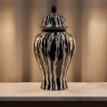 A glossy black and white zebra-print lidded ginger jar vase displayed on a white marble console table in a warmly lit interior setting.