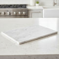 A rectangular white marble cutting board with natural gray veining, resting on a matching white marble kitchen countertop with a blurred modern kitchen background.