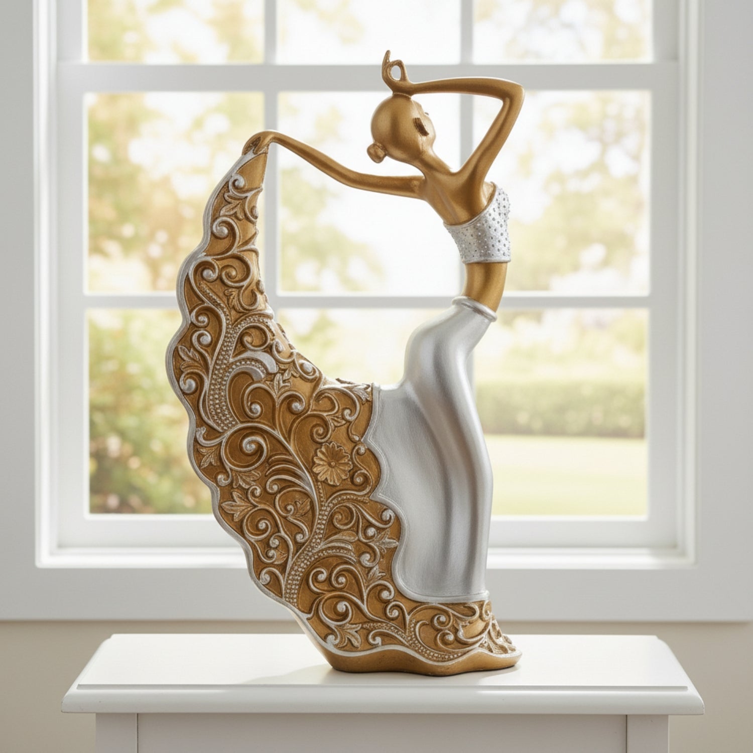 A decorative figurine of a dancing woman with a flowing skirt, styled in metallic gold and silver, displayed on a white table in front of a bright window.