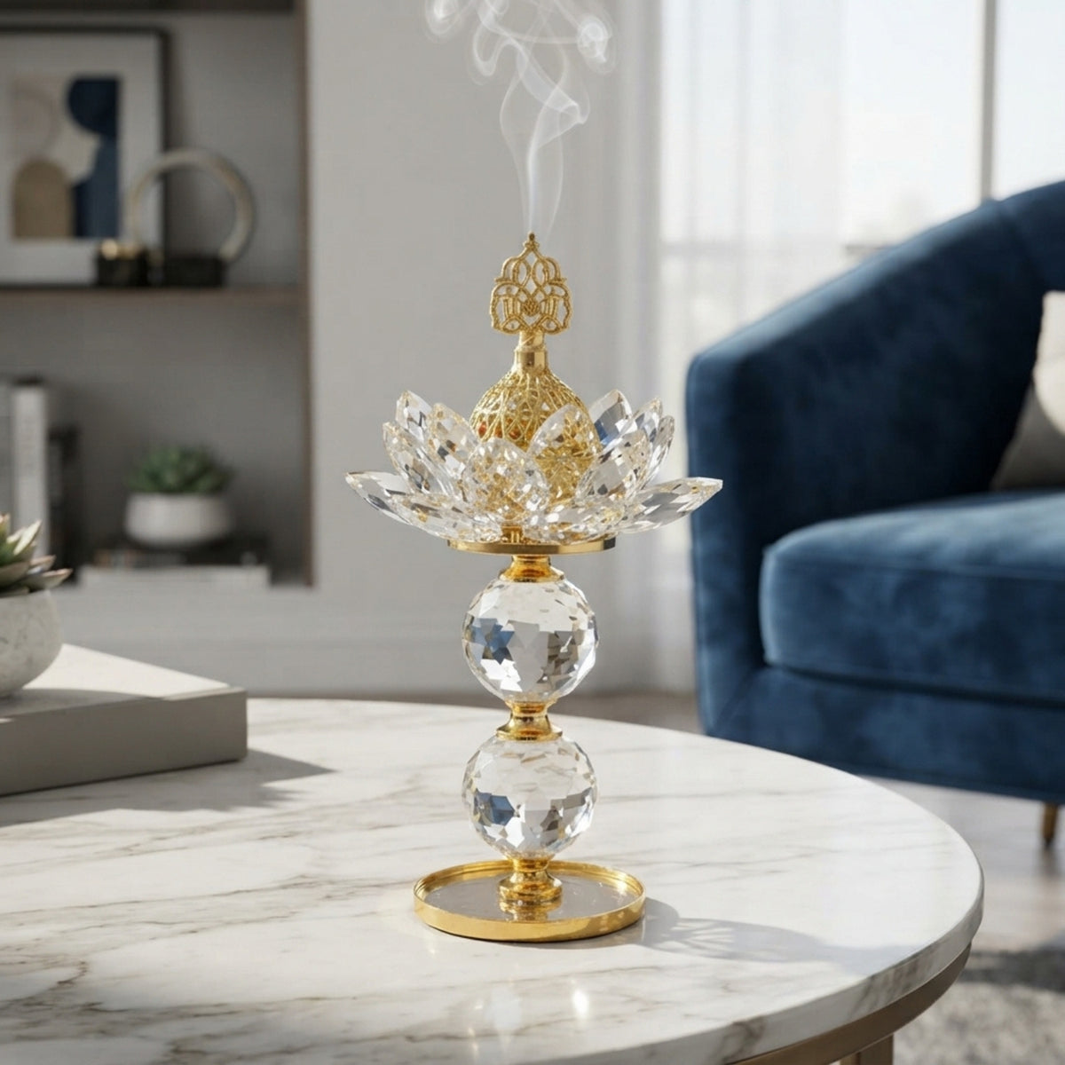 A gold and clear crystal lotus incense burner sits on a white marble round table in a bright, modern living room with a blue velvet armchair in the background.