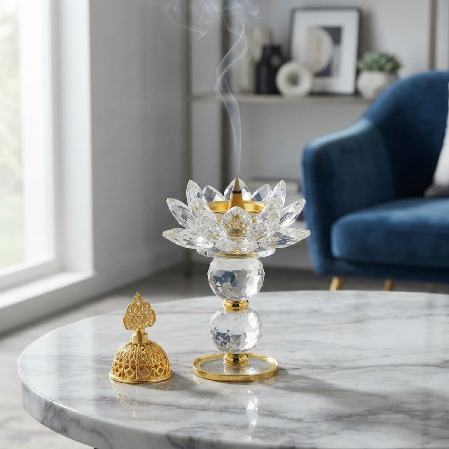 A clear crystal lotus-shaped incense holder with gold-tone accents sits on a round marble table, with smoke rising from the top. A matching gold incense burner rests beside it.
