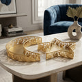 Gold decorative trays with intricate cutout patterns, including a star-shaped tray and a crescent-shaped tray, displayed on a light marble coffee table in a modern living room setting.