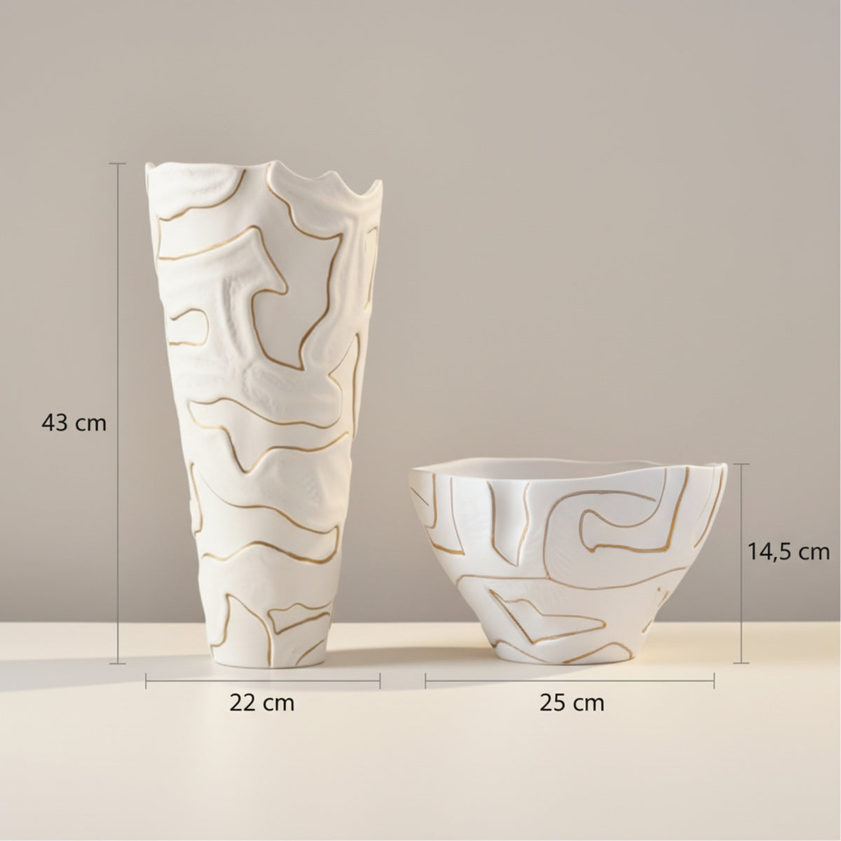 Two white ceramic decorative vases with gold abstract line patterns, shown with dimension labels: a tall vase measuring 43 cm in height and 22 cm in width, and a shallow bowl-shaped vase measuring 14,5 cm in height and 25 cm in width, on a light beige surface against a warm gray background.