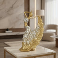 A decorative figurine of a dancing woman in a flowing dress, shown on a marble-topped table in a modern living room setting. The figurine features a metallic gold body and wings with a textured silver-white dress.