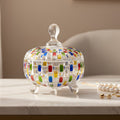 A clear glass lidded candy dish with colorful mosaic tile accents on the body and lid,