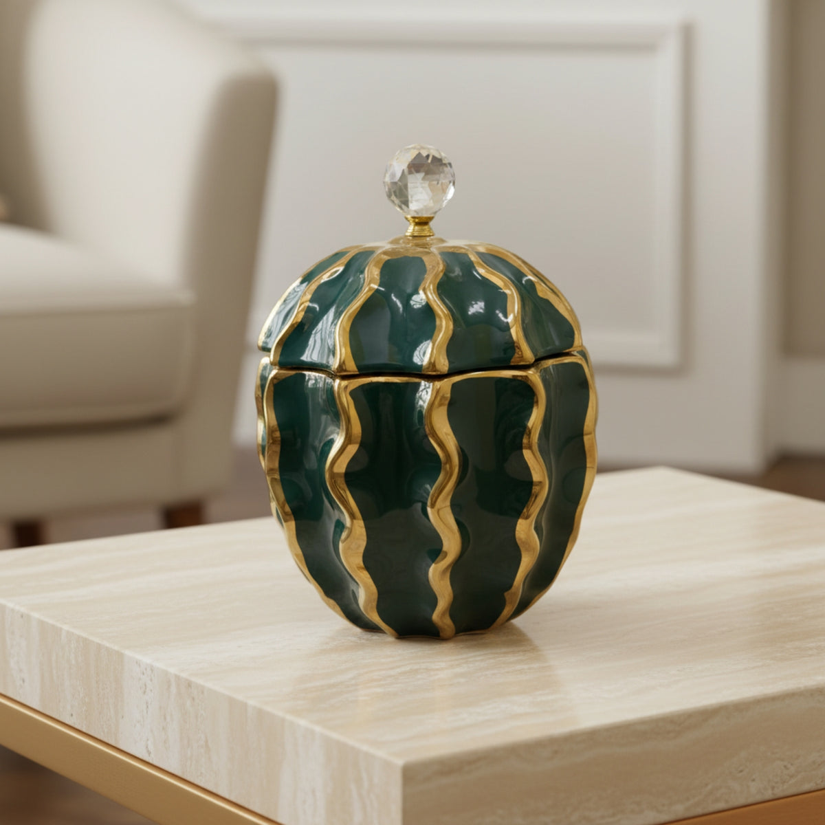 A decorative lidded container with a rounded, ribbed design in glossy dark green and gold, topped with a clear crystal knob, displayed on a light wood table in a modern living room setting.