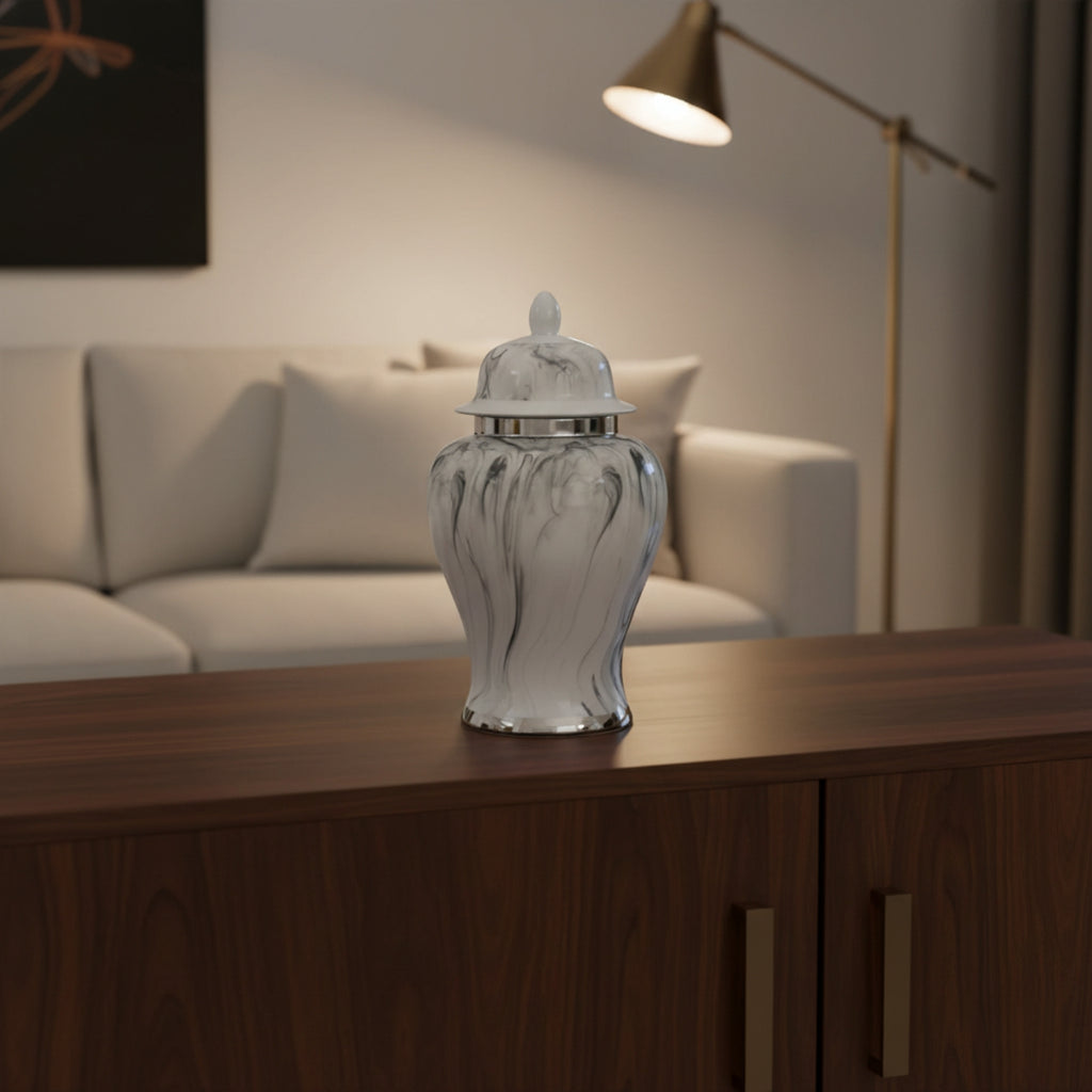 A white and gray marbled glass jar with a matching lid sits on a dark wood sideboard in a modern living room setting with a sofa and floor lamp in the background.