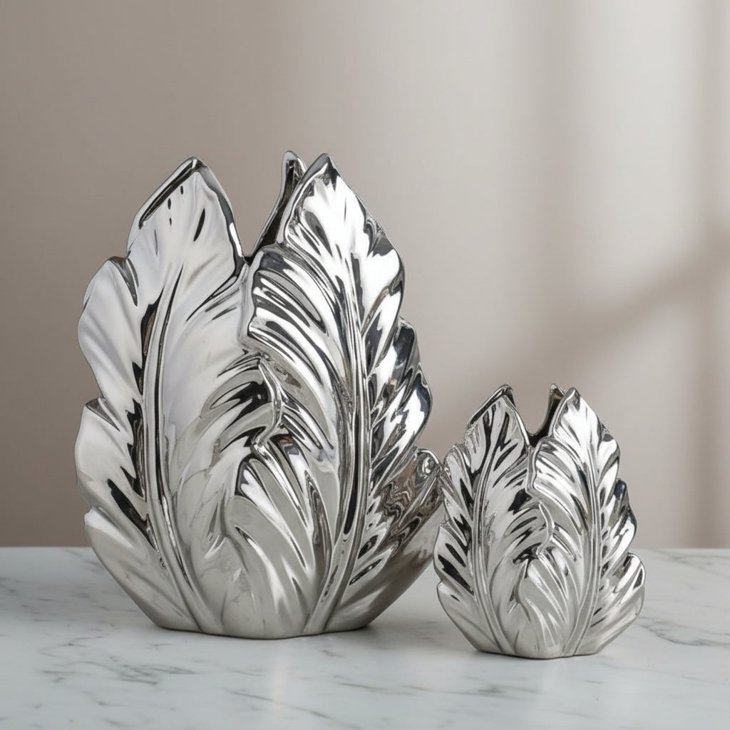 Two silver leaf-shaped vases on a marble surface with a neutral background