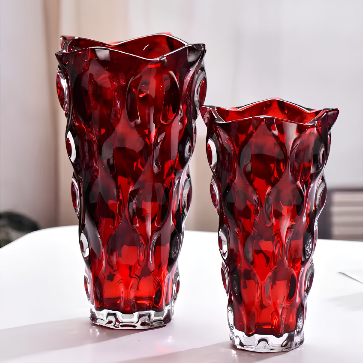 Two red glass vase-like containers with wavy scalloped rims and an embossed bubble pattern, displayed on a white surface against a soft light gray background.