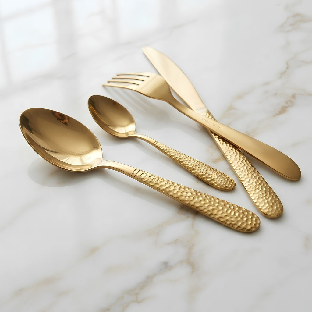 Four-piece gold-toned cutlery set with a polished finish and textured handles, arranged on a white marble surface.