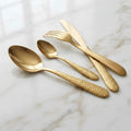 Four-piece gold-toned cutlery set with a polished finish and textured handles, arranged on a white marble surface.