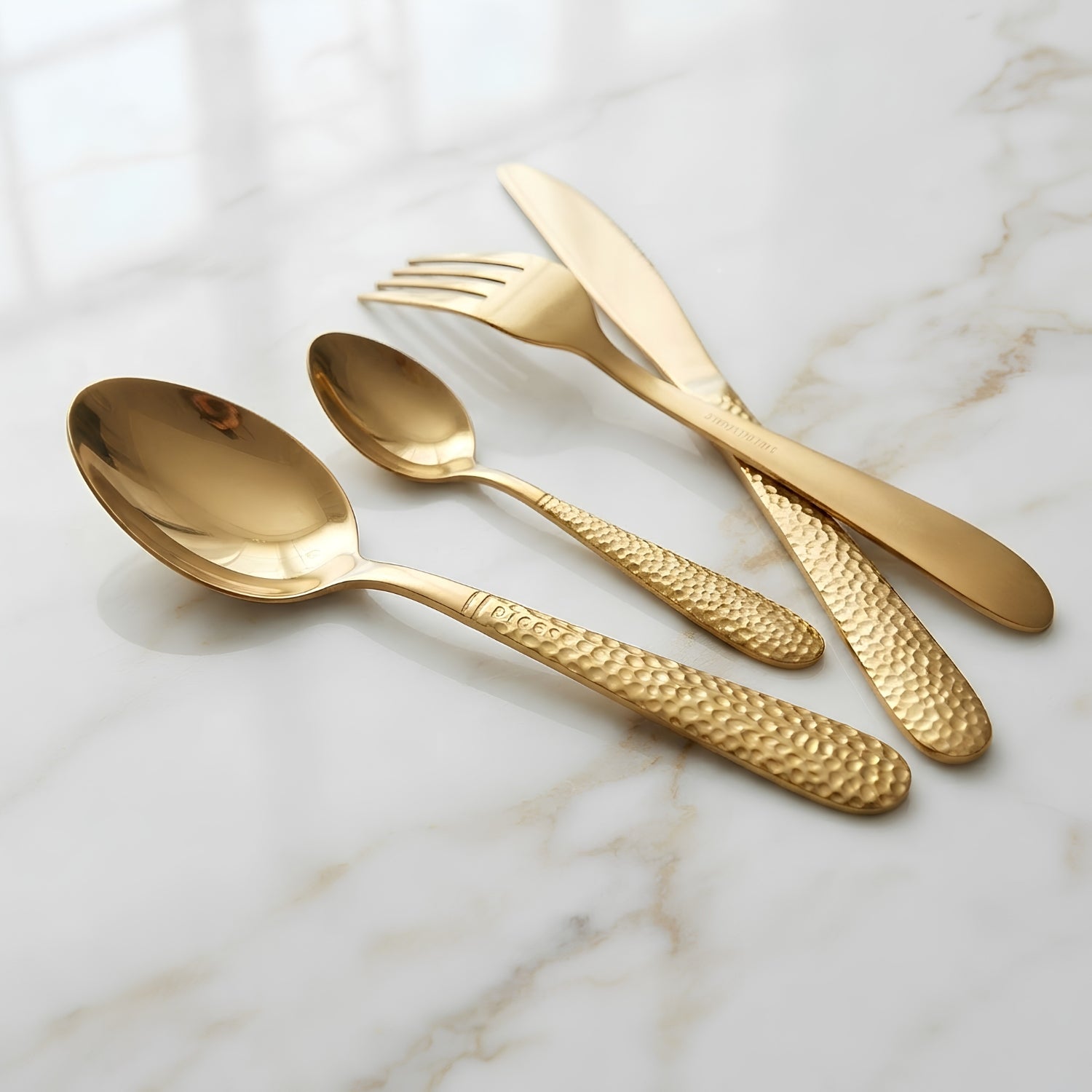 Four-piece gold-toned cutlery set with a polished finish and textured handles, arranged on a white marble surface.