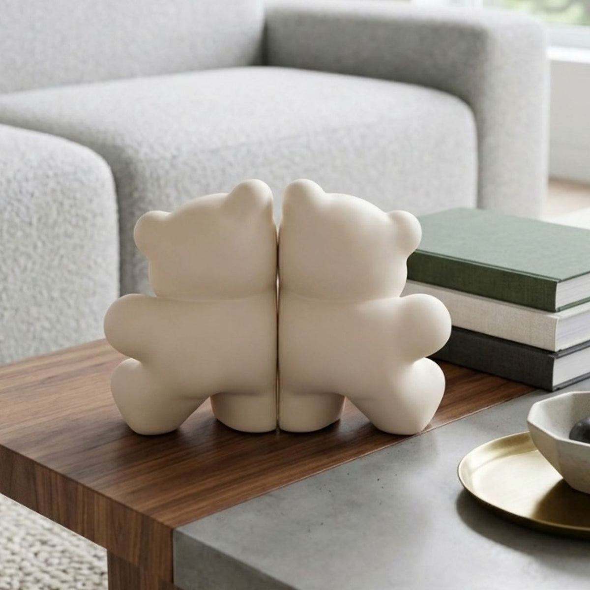 A pair of cream-colored bear-shaped bookends shaped like their backs, displayed on a wooden coffee table next to stacked books in a modern living room setting.