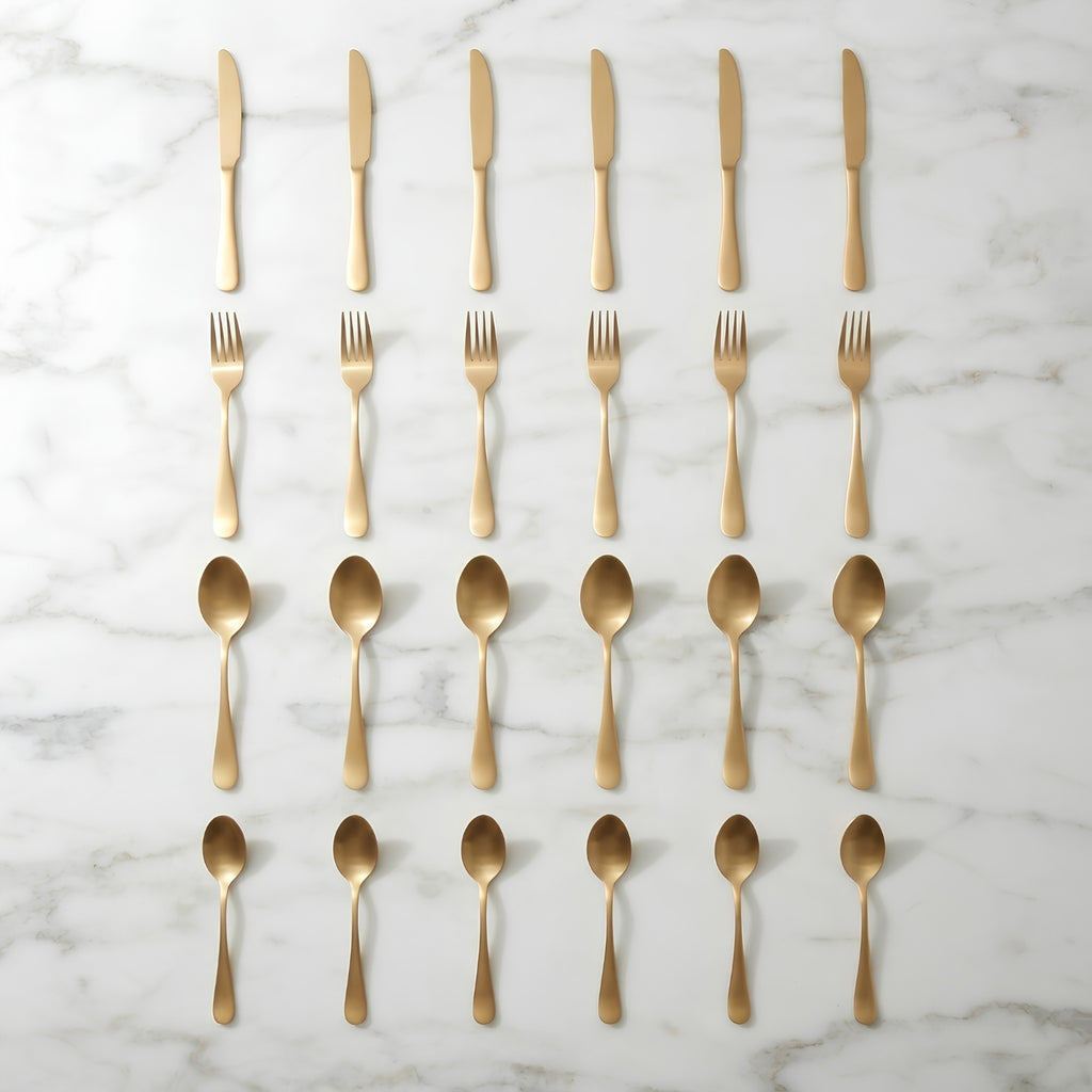 Gold-colored flatware set including knives, forks, and spoons, neatly arranged in rows on a white marble background.