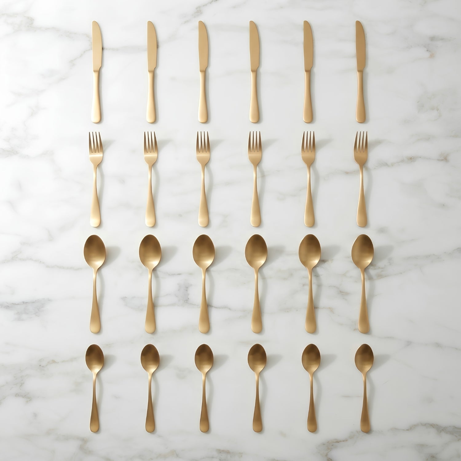 Gold-colored flatware set including knives, forks, and spoons, neatly arranged in rows on a white marble background.