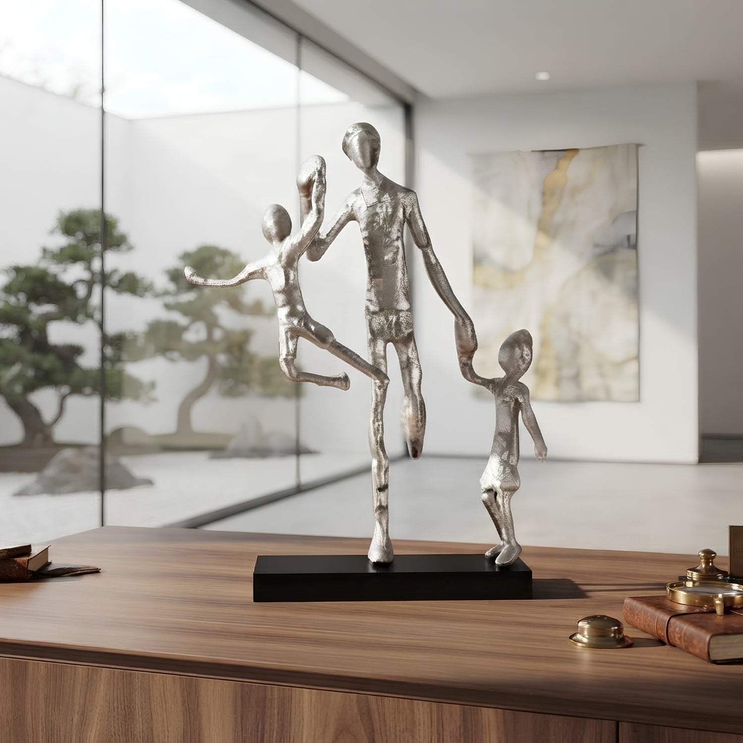 A metallic silver family sculpture of three abstract figures standing on a black rectangular base, displayed on a wooden console table in a modern interior setting.