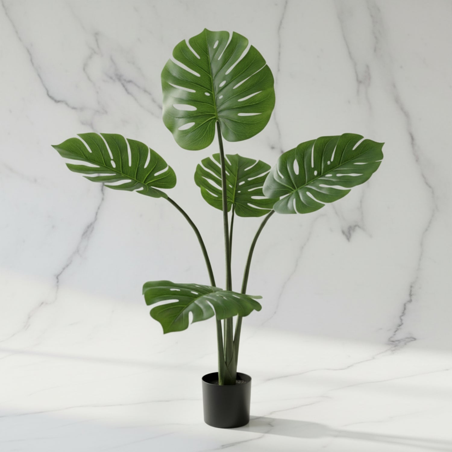 An artificial monstera plant with realistic green leaves in a black pot, set against a white marble background.