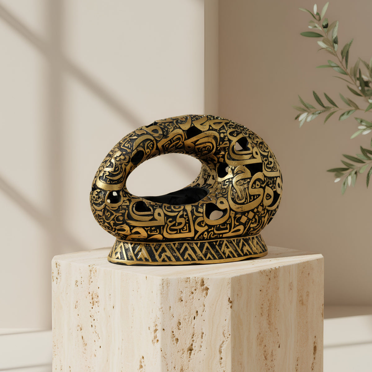 An ornate black and gold decorative ring-shaped sculpture with intricate cutout patterns, displayed on a light beige stone pedestal in a softly lit interior setting.