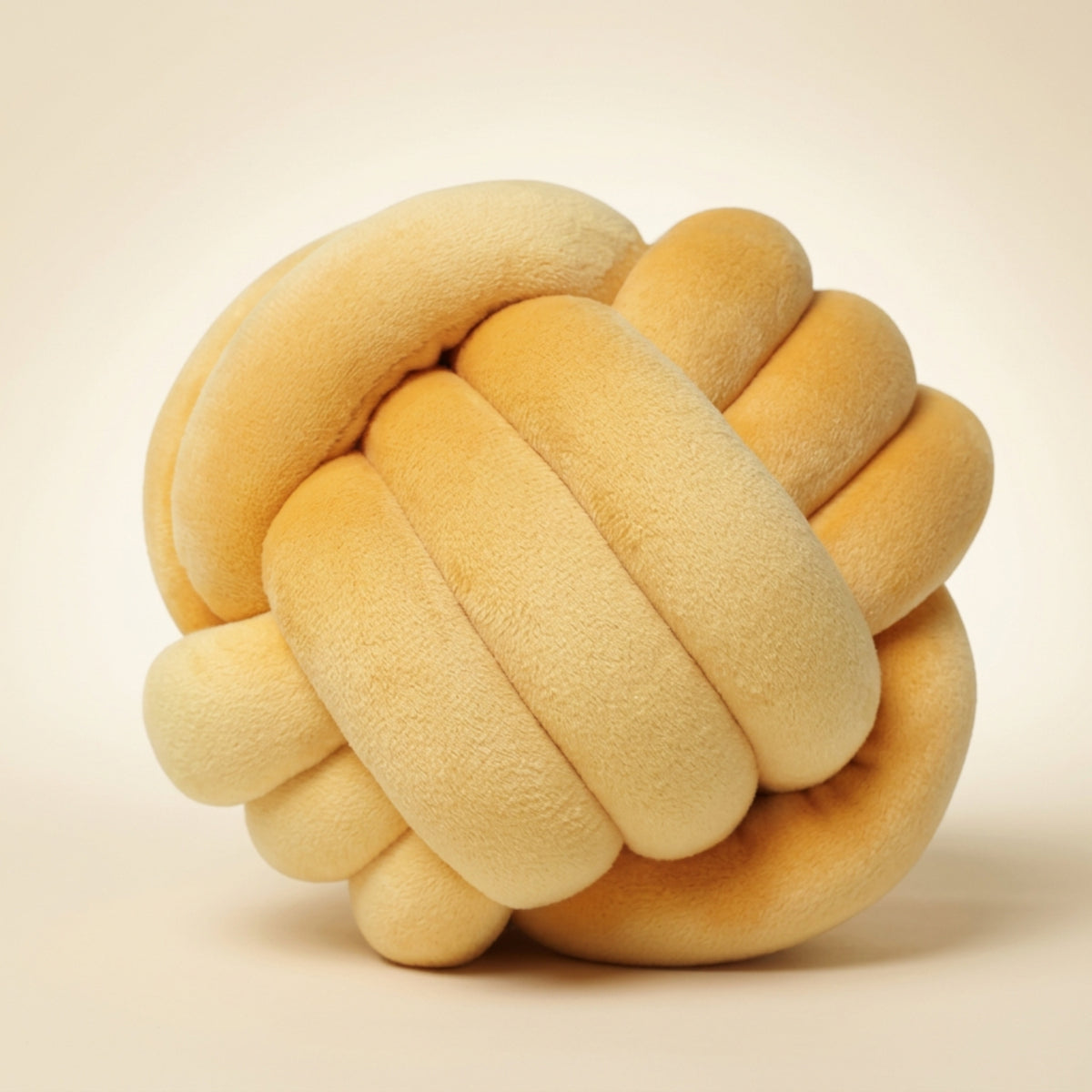 A plush, knot-shaped decorative pillow in a warm cream-beige color, photographed against a solid, light beige background.