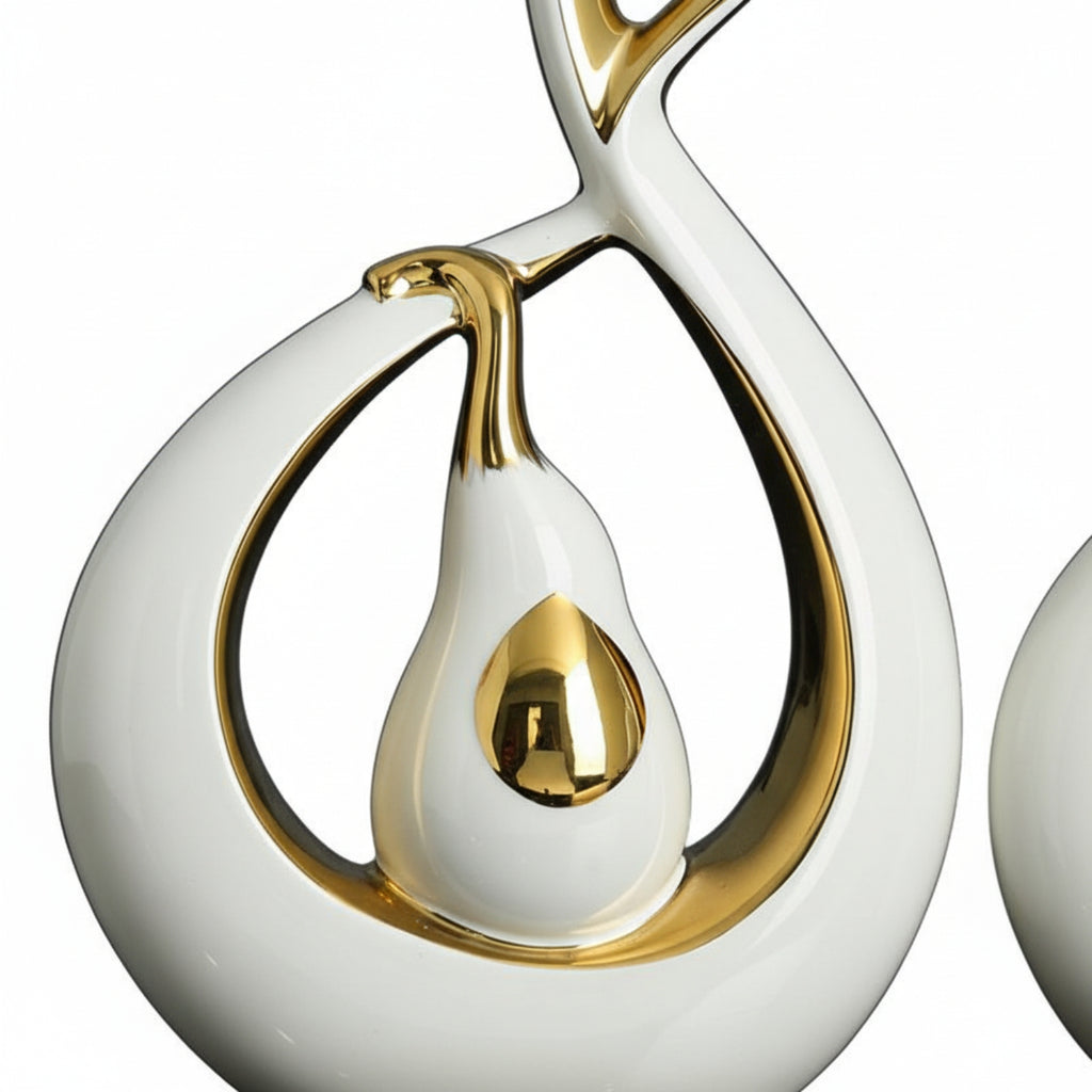 A close-up of a glossy white and gold abstract sculptural object on a white background, with part of a matching object visible at the right edge.
