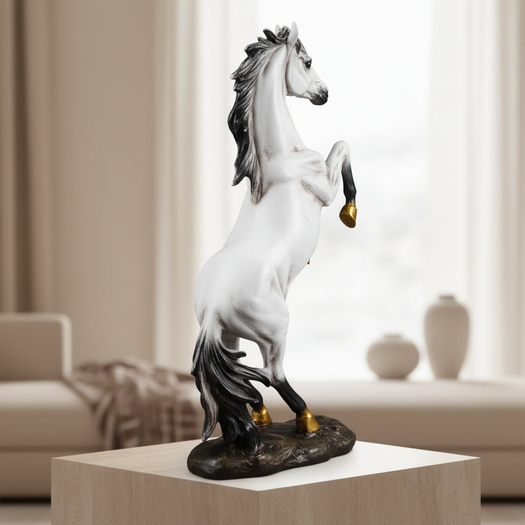 A rearing white horse statue with black mane, tail, and lower legs, plus small gold hooves, displayed on a pedestal in a softly lit living room setting.