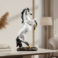 A white and black rearing horse figurine with gold-colored hooves, displayed on a white marble table in a modern, softly lit room.