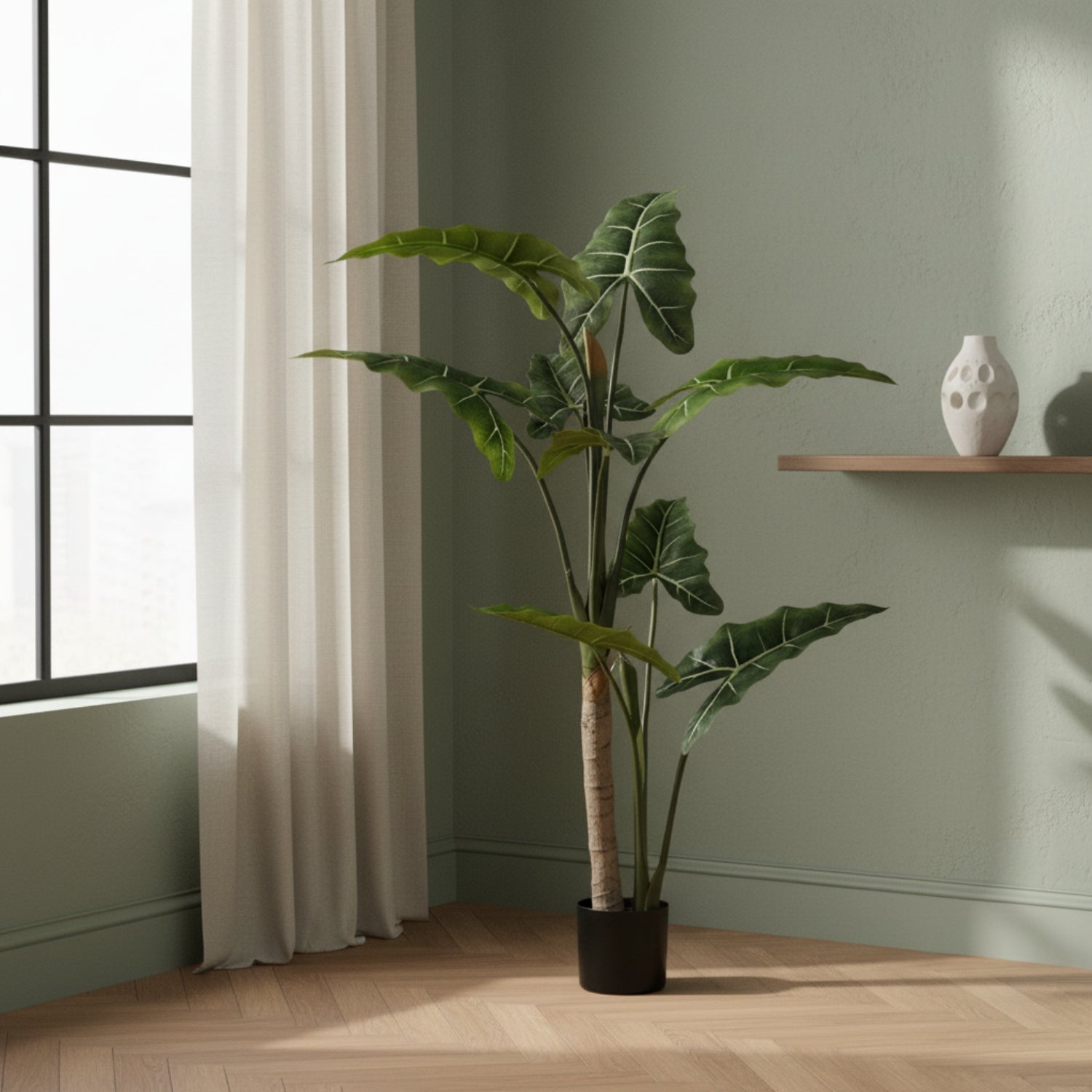 A tall artificial potted plant with large green tropical leaves stands in a room corner beside a window with a curtain, next to a light wood shelf holding a white vase.