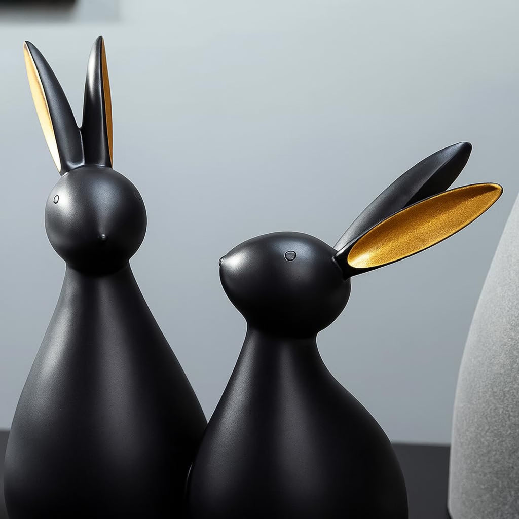 Two matte black rabbit-shaped decorative sculptures with glossy gold inner ears, shown against a soft gray background.